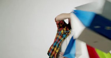 Renkli tişörtlü adam alışveriş torbalarını tutarken ve sallarken mutlu bir şekilde dans ediyor. Başarılı bir alışveriş çılgınlığının heyecanını beyaz bir arka plana yansıtıyor. Perakende ve tüketim için harika.,