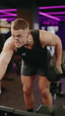 Kararlı bir erkek sporcu modern bir spor salonunda dambıl kürek çekiyor. Gücünü ve gücünü geri kazanmaya odaklanıyor. Bu fitness videosu kendini adamışlık ve canlı bir yaşam tarzı sergiliyor.,