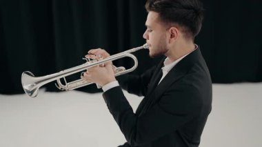 Modern bir stüdyoda siyah arka planda trompet çalan bir erkek caz şarkıcısı. Canlı caz konseri. Müzik tutkusu. Genç trompetçinin yakın eli. Müzik odası.