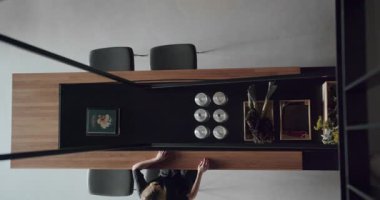 Kadın modern ve geniş ahşap mutfak odasında sandalyede oturuyor. Gayrimenkul. Üst Manzara. Ahşap adası ve sandalyeleri olan lüks bir mutfak. Lüks evde modern iç mekan. Neoklasik biçim, samimi iç mekan