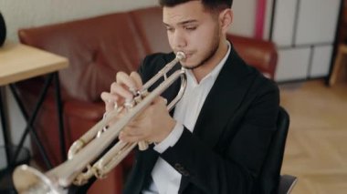 Takım elbiseli genç ve yakışıklı bir adam arzu ve ilhamla trompet çalar. Canlı caz konseri. Müzik tutkusu. Genç trompetçinin yakın eli. Müzik odası.