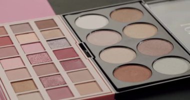 İki profesyonel makyaj paleti, çıplak göz farı ve fosforlu kalemler, farklı güzellikler yaratmak için çeşitli parıltı ve mat gölgeleri göstererek yavaşça dönüyor.