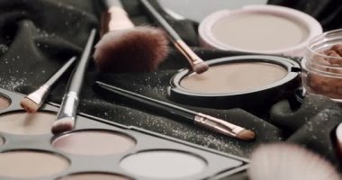 Parlak siyah bir kumaşın üzerinde duran göz kamaştırıcı makyaj ürünleri ve kozmetik fırçalar. Pudra da dahil olmak üzere çeşitli güzellik gereksinimleri. Vakıf. Ve mükemmel bir görünüm için göz farı paleti