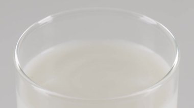 Dolu bir bardağa düşen tek bir damla sütün makro yavaş çekim gücü beyaz sıvı yüzeyde beyaz bir zemin üzerinde güzel bir taç sıçraması ve dalgalanmalar yaratıyor..