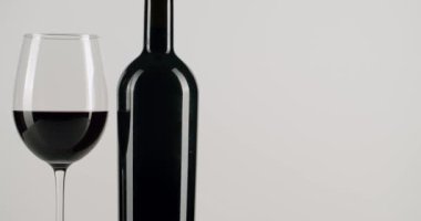 Zengin kırmızı şarapla dolu zarif bir bardak, siyah bir şişenin önünde, temiz bir şişeye karşı yavaşça dönüyor. Bu sofistike kompozisyon kutlama, lüks, yemek, kaliteli şarap yapımı için mükemmeldir.