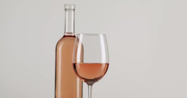 Zarif bir gül şarabı kristal bir bardağın içinde kıvrılarak eşleşen bir şişenin yanına yerleştirilmiş, temiz beyaz bir arka planda izole edilmiş..