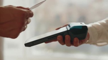 Bir müşterinin, modern ve kullanışlı bir nakit ödeme metodunu temsil eden bir işlemi tamamlamak için bir kasiyer tarafından tutulan POS terminalinden kredi kartı geçirmesi.