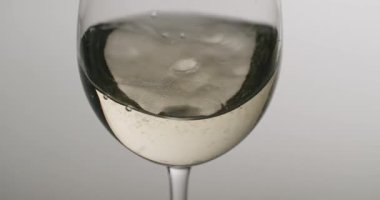 Yavaş çekimde dönen beyaz şarapla dolu kristal berrak bardak, altın sıvının yüzeyinde zarif dalgalar ve dalgalanmalar yaratıyor, camın üzerinde küçük kabarcıklar oluşuyor.