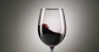 Zarif bir kırmızı şarap kadehi dairesel bir hareketle pürüzsüz, mezun olmuş gri bir arka plana doğru dönüyor, güzel dalgalar yaratıyor ve içeceğin derin rengini ve viskozitesini vurguluyor.