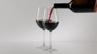 Sommelier, romantik bir akşam yemeği için siyah bir şişeden kırmızı şarabı yansıtıcı bir masanın üstünde iki kristal şarap bardağına dolduruyor.