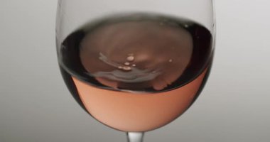 Son damla gül şarabının son damlasına yakın çekim kristal bir bardağa düşerek temiz, izole bir açık gri zemine karşı zarif dalgalanmalar ve sıçramalar yaratır..