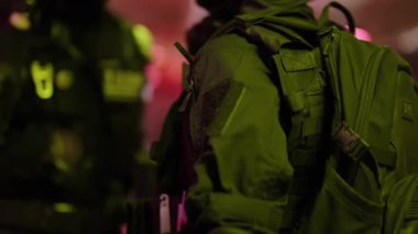 Silahlı özel kuvvetler askerlerinin tam taktik teçhizatlı, başlıklı ve kar maskeli ağır çekimleri yeşil ve pembe ortam aydınlığı olan karanlık bir ortamda görev için hazır bekliyor.