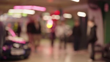 Bir gece araba şovu sırasında kalabalık bir yeraltı otoparkında yürüyen isimsiz insanlar, canlı neon ışıklarıyla kasıtlı olarak bulanık çekimde sinematik bir bokeh etkisi yaratıyor.