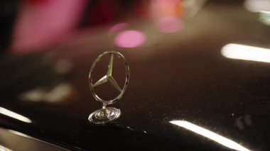 Chisinau Moldova 12.12.2026. Lüks bir Alman arabasının parlak siyah kaputunun üzerindeki krom Mercedes-Benz yıldız amblemine yakın plan, ışık yüzeyini güzel bir bokeh arka planda yansıtıyor