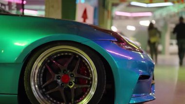 Bukalemun yanardöner boyalı, özel olarak modifiye edilmiş spor bir arabanın yakın görüntüsü. Alaşımlı tekerlek ve kırmızı fren kalibrelerini parlak bir yeraltı garajında park halindeyken gösteriyor.