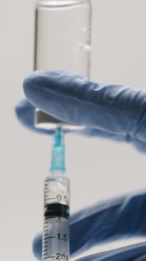 Mavi eldivenli bir tıp uzmanının, aşı ya da tedavi için temiz, beyaz bir arkaplan eşliğinde cam şişeden şırıngaya sıvı ilaç çekmesi.