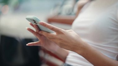 Genç bir kadının yakın çekimde manikürlü elleri dışarıda otururken cep telefonuna yazarken modern iletişim teknolojisini ve dijital yaşam tarzını gösteriyor.