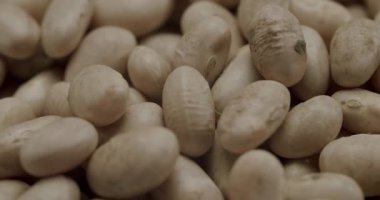Beyaz cannellini fasulyeleri kaseye düşüyor. Yavaş çekim, beyaz cannellini fasulyelerinin seramik bir kaseye düşüşünün yukarıdan aşağı görüntüsü, temiz beyaz arkaplana karşı ağzına kadar doluyor.