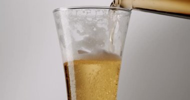 Bira şişeden bardağa yavaş çekimde dökülüyor, kalın beyaz köpük ve baloncuklardan bir kafa oluşturuyor, sahnenin tamamı sade beyaz bir arka planda izole ediliyor.