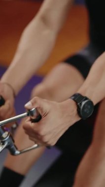 Spor salonundaki kürek çekme makinesinde çalışan adam. Kürek çeken bir adamın ellerini yakın plan çekimde çekiyoruz. Antrenmandaki ritmik hareket ve çabaya odaklanıyoruz..