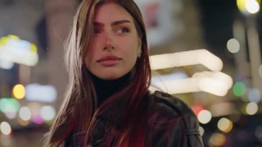 Gece lambalarının arka planında genç bir kadının portresi. Geceleri şehir merkezinde poz veren güzel bir kadın. Sokaktaki doğal güzellik kraliçesi. Yavaş çekim.