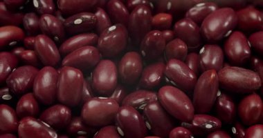 Ağır çekimde dönen kırmızı fasulyelerin detaylı makro görüntüsü, sağlıklı pişirme kavramları ve beslenme bilgileri için arka plan olarak dokularını ve derin renklerini vurguluyor