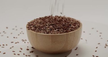 Beyaz bir zemin üzerinde ahşap bir kasede dönen doğal kahverengi keten tohumlarının makro görüntüsü, sağlıklı bir diyet, vejetaryen yaşam tarzı ve süper gıda besinleri için dokularını ve faydalarını vurguluyor..