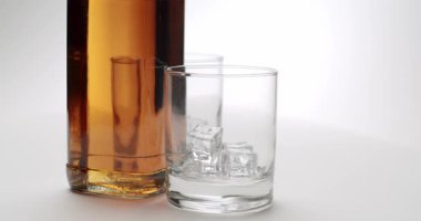 Altın viski şişesi. İçi buz dolu iki zarif bardak. Temiz, izole edilmiş beyaz bir arkaplanda yavaşça dönüyor..