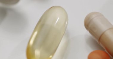 Çeşitli renkli ilaç hapları, haplar ve kapsüller yavaş yavaş temiz beyaz bir yüzeye yayılıyor, birçok farklı hap, kapsül, sağlık hizmetlerini, farmakolojiyi ve tıbbi tedaviyi sembolize ediyor.