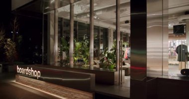 Modern Board Shop Storefront at Night. Stylish store with plants and clothing. This trendy shop attracts customers with its unique style and modern design. Boardshop exterior at night.