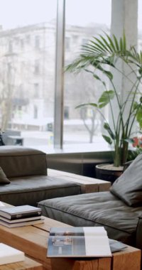 Rahat mobilyaları ve şehir manzarası olan modern ofis. Doğal ışıkla iç içe. Kitaplar ve dergiler ahşap bir masada sergilenerek rahatlatıcı ve üretken bir atmosfer yaratıyor..