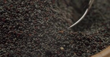 Haşhaş tohumları karıştırılıyor ve ahşap bir kasede metal bir kaşık tarafından kepçeleniyor. Ağır çekimde, yemek pişirmede kullanılan küçük, yenilebilir tanelerin dokusunu ve hareketini gösteriyor.