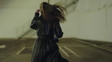 Deri ceket giyen genç bir kadın şık marka güneş gözlükleriyle fotoğraf çekimi için poz veriyor. Gece sokakta poz veren şık bir kadın. Yeraltı otoparkında poz veren uzun saçlı genç bir kadın model..