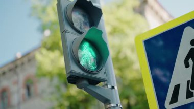 Yürüyen bir insan sembolü yanıp sönen yeşil yaya ışığı ışığına yakın durmak, yolu geçmenin güvenli olduğunu gösterir, güneşli bir günde yakınlarda bir yaya geçidi tabelası görünür.