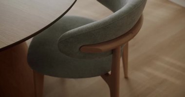 Yuvarlak ahşap bir masanın yanında zarif, gri döşemeli bir sandalye olan modern bir yemek odası manzarası. Çağdaş iç tasarım ve mobilya işçiliğinin vurgulanması