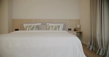 Modern ve rahat bir yatak odası, büyük bir yatak odası, ahşap bir yatak başlığı ve başucu, ve başucu masa, pencereden hafif bir esinti saf beyaz perde hareket ederken, huzurlu ve rahatlatıcı bir atmosfer yaratıyor