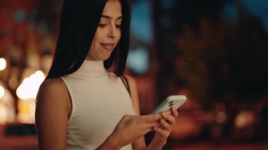 Uzun siyah saçlı çekici bir kadın cep telefonunu kullanırken gülümsüyor ve arka planda büyülü bir atmosfer yaratıyor.