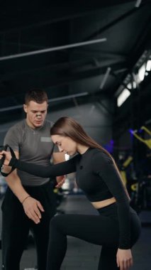 Modern bir spor salonunda zorlu bir uzaklaştırma antrenmanı sırasında genç bir kadına antrenörlük yaparak formda ve en uygun sonuç için tekniğini korumasına yardımcı oluyor. dikey