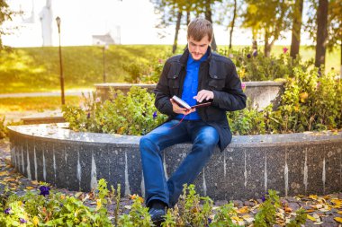 Bir kitapla parkta oturan adam