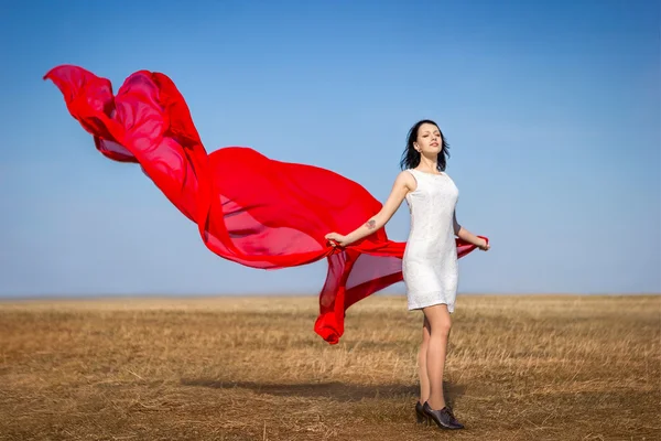 Девушка в белом платье с красной тканью на поле — стоковое фото