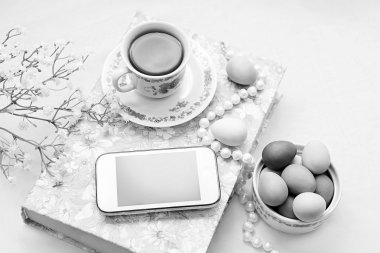 Bir fincan çay ve bir beyaz saten zemin üzerine çiçekli inci kolye ile telefon. Bir kitap, çay bardağı, telefon ve dekorasyon.