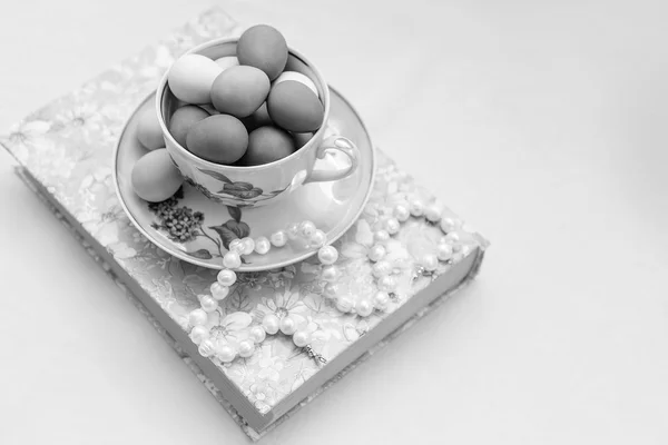 Algunos platos con huevos de Pascua pintados y perlas en un libro con flores de lavanda sobre fondo blanco — Foto de Stock