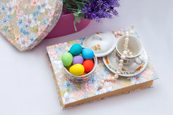 Una taza y un platillo con huevos de Pascua pintados y perlas en el libro sobre fondo blanco — Foto de Stock