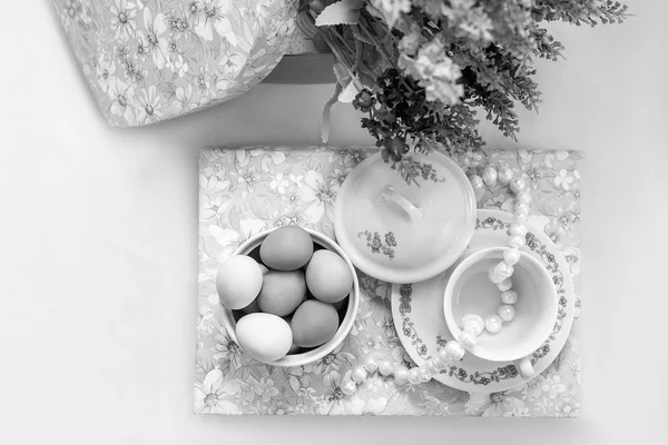 Algunos platos con huevos de Pascua pintados y perlas en un libro con flores de lavanda sobre fondo blanco — Foto de Stock