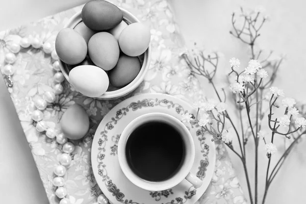 Une tasse de thé avec des œufs peints de Pâques et quelques décorations fleurs, collier de perles et un livre . — Photo