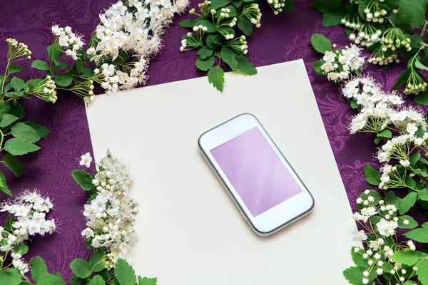 Hermosas ramas florales y un teléfono blanco sobre un fondo de papel texturizado y tela púrpura oscura — Foto de Stock