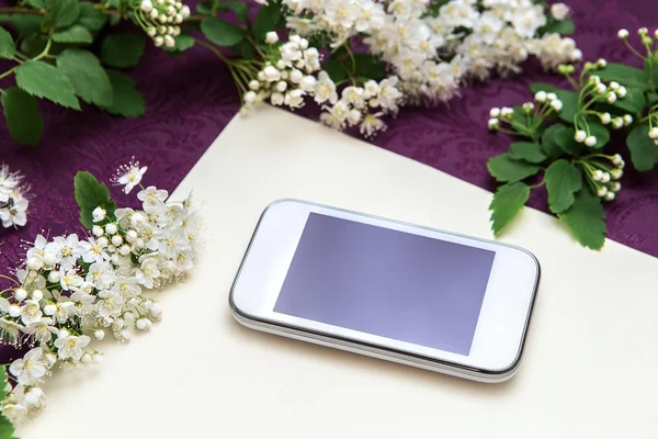 Hermosas ramas florales y un teléfono blanco sobre un fondo de papel texturizado y tela púrpura oscura — Foto de Stock