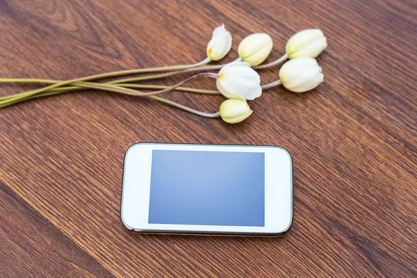 Teléfono móvil con flores blancas sobre fondo de madera — Foto de Stock