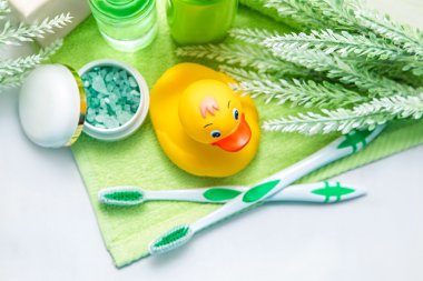 Yeşil havluyla banyo aksesuarları. Lastik ördek, diş fırçası, deniz tuzu, sabun ve losyon. Banyo için bebek bakım aksesuarı. Çocuklar için sarı ördek yavrusu.