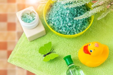 Yeşil havluyla banyo aksesuarları. Lastik ördek, diş fırçası, deniz tuzu, sabun ve losyon. Banyo için bebek bakım aksesuarı. Çocuklar için sarı ördek yavrusu.